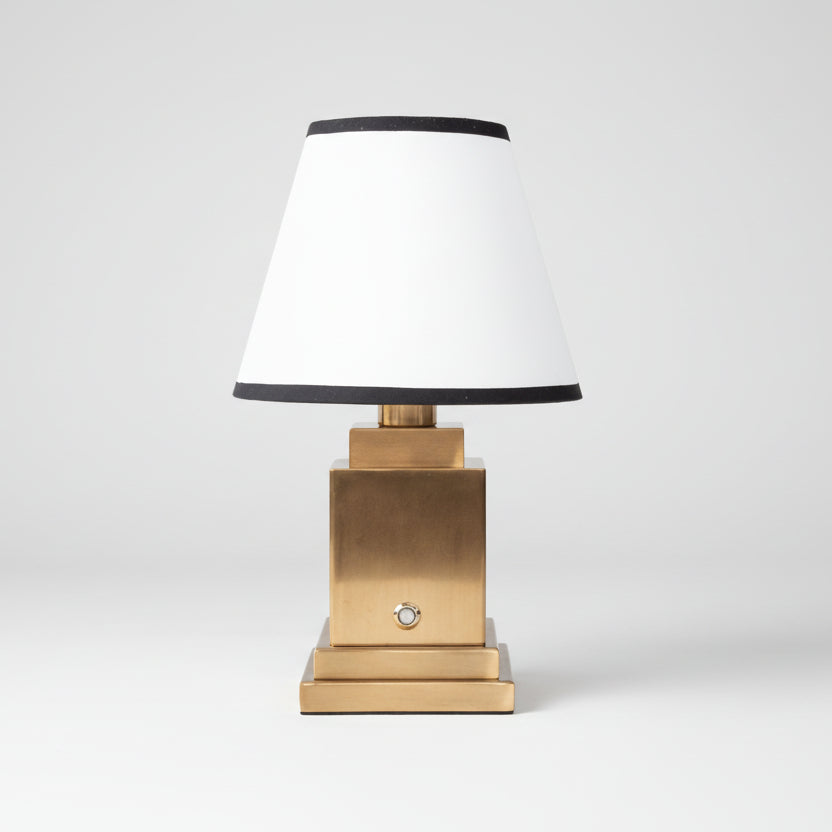 Lampe de chevet luxueuse avec base carrée en laiton doré et abat-jour blanc bordé de noir, luminaire classique chic pour chambre d'hôtel ou bureau.