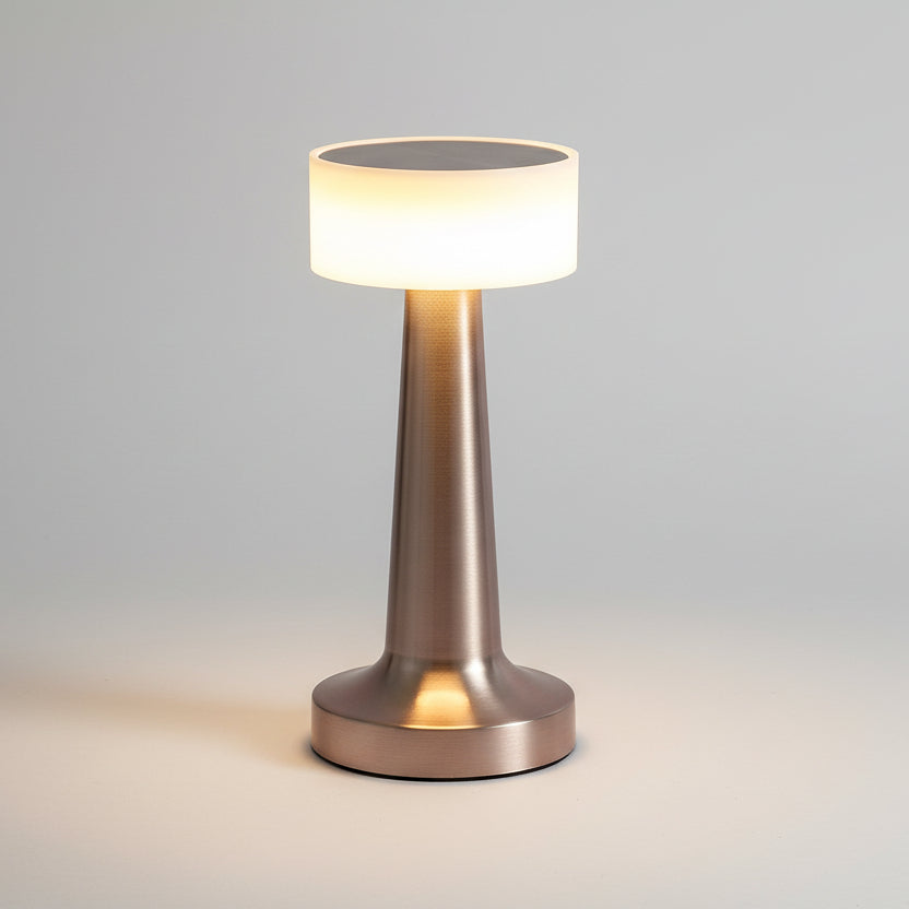 Lampe de table LED rechargeable sans fil en laiton gris brossé, dotée d'un abat-jour cylindrique lumineux et d'un pied conique élégant, idéale pour une ambiance tamisée en restaurant ou sur une table de chevet.