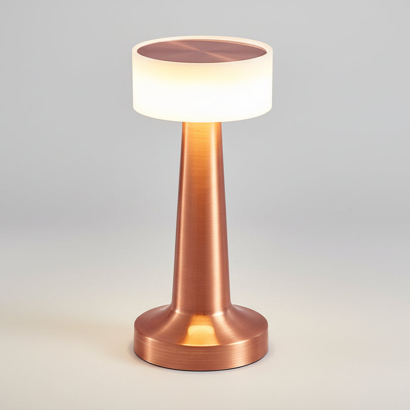 Lampe de table LED rechargeable sans fil en laiton rose brossé, dotée d'un abat-jour cylindrique lumineux et d'un pied conique élégant, idéale pour une ambiance tamisée en restaurant ou sur une table de chevet.