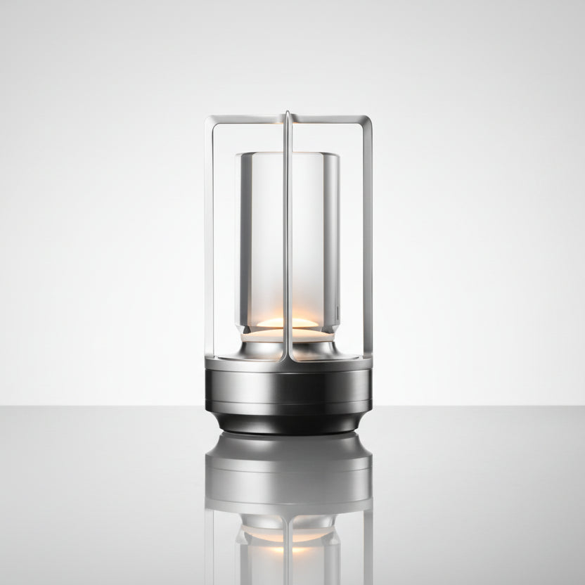 Lampe lanterne LED sans fil haut de gamme avec diffuseur en verre cylindrique et structure minimaliste en laiton argent, luminaire rechargeable pour ambiance luxueuse en intérieur ou extérieur abrité.